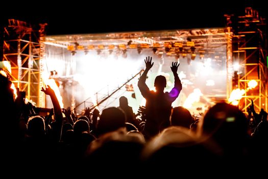 Silhouettes of people with raised hands at a concert. Stage light