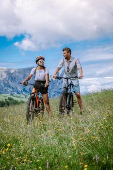 couple men and woman on vacation in the Dolomites Italy, Alpe di Siusi, men and woman on Mountainbike - Seiser Alm with Sassolungo - Langkofel mountain group in background at sunset Europe