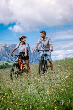 couple men and woman on vacation in the Dolomites Italy, Alpe di Siusi, men and woman on Mountainbike - Seiser Alm with Sassolungo - Langkofel mountain group in background at sunset Europe