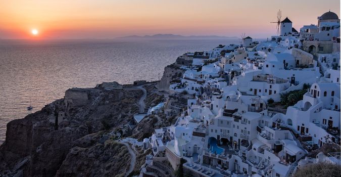 Sunset at the Island Of Santorini Greece, beautiful whitewashed village Oia with church and windmill during sunset, streets of Oia Santorini during summer vacation at the Greek Island