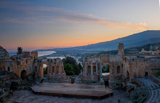 Ruins of Ancient Greek theatre in Taormina on background of Etna Volcano, Italy. Taormina located in Metropolitan City of Messina, on east coast of island of Sicily Europe