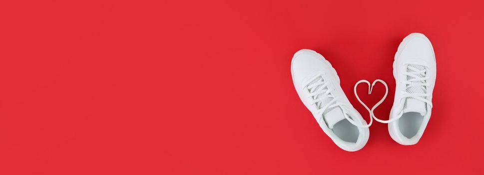 White sports shoes and heart shape from laces on a red background. Simple flat lay banner with copy space.