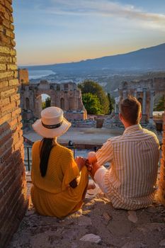 couple men and woman visit Ruins of Ancient Greek theatre in Taormina on background of Etna Volcano, Italy. Taormina located in Metropolitan City of Messina, on east coast of island of Sicily Italy