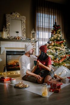 Cute, young couple by fireplace with a Christmas tree,Family sitting on a floor. Couple near christmas tree with candle lights