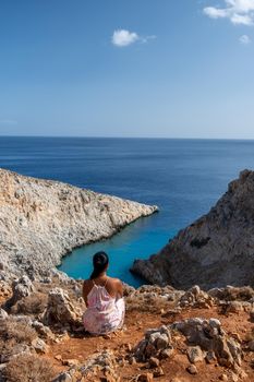 Crete Greece Seitan Limania beach with huge cliff by the blue ocean of the Island of Crete in Greece, Seitan limania beach on Crete, Greece. Europe young woman mid age asian looking out over ocean during vacation