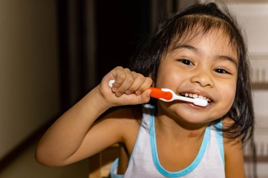 Little asian girl kid while brushing her teeth. Child while enjoying brushing her teeth