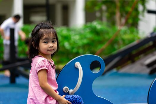 Pretty asian little girl while sitting and playing on a see saw in a playground