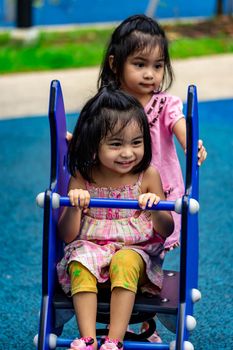 Pretty asian little twins girls while sitting and playing on a see saw in a playground