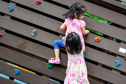 Pretty asian little twins girls while climbing in a playground and helping each other