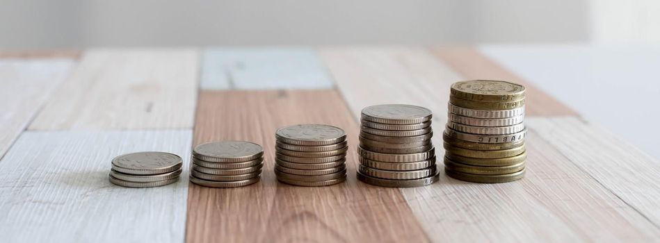 Savings, increasing columns of coins isolated on white background and wooden table. Financial growth