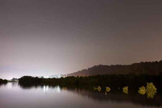 Landscape view of lakes, nature and mountains during night with clear bright sky with stars and bright lights reflecting on water somewhere in Asia