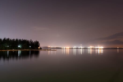 Coastline view of sea, pier, sky during dusk with lights reflection on water somewhere in Asia