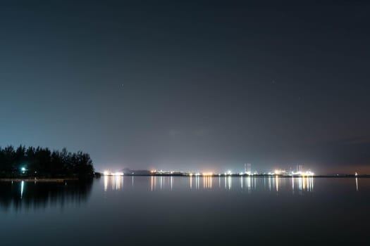 Coastline view of sea, pier, sky during dusk with lights reflection on water somewhere in Asia