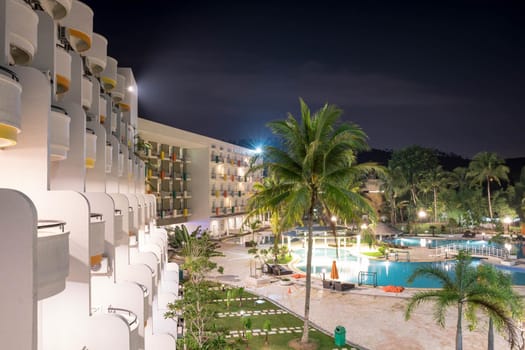 Hotel balcony side view of a hotel resort during night with swimming pool and bright lights reflecting on blue swimming pool water long exposure somewhere in Asia