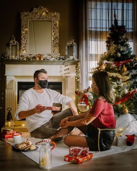 Christmas couple wearing mask during Christmas night,Close up portrait of happy mixed-races couple with christmas presents and wearing medical masks in quarantine. couple with face mask during covid outbreak pandemic