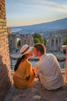 couple men and woman visit Ruins of Ancient Greek theatre in Taormina on background of Etna Volcano, Italy. Taormina located in Metropolitan City of Messina, on east coast of island of Sicily Italy