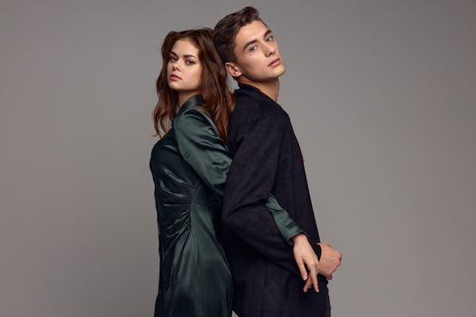 A man in a suit stands with his back to a woman in a dress on a gray background and holds hands. High quality photo