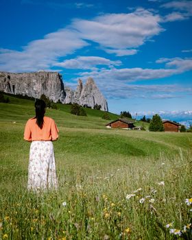 Alpe di Siusi - Seiser Alm with Sassolungo - Langkofel mountain group in background at sunset. Yellow spring flowers and wooden chalets in Dolomites, Trentino Alto Adige, South Tyrol, Italy, Europe. Summer weather with dark clouds rain, couple men and woman on vacation in the Dolomites Italy