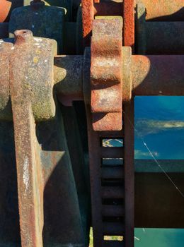 In the foreground a rusty toothed geared device and a little  thread of spider's  web, in the background a blue riverside.Vertical composition