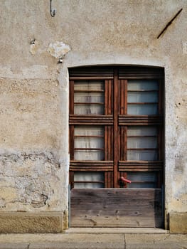 Facade of an urban house with wooden door and a small window datable to the '60s.Time and carelessness have ruined the wood and the wall plaster.