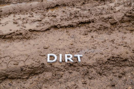 the word dirt laid with silver letters on wet dirt road surface - close-up with selective focus.