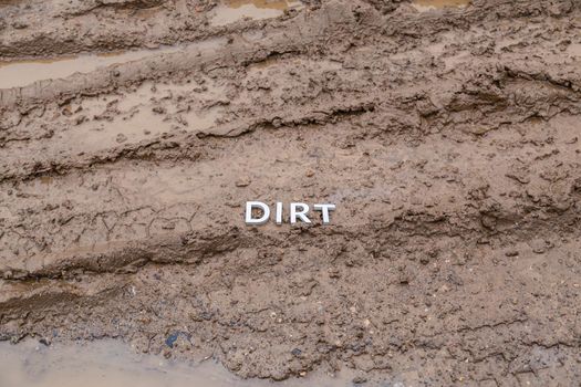 the word dirt laid with silver letters on wet dirt road surface - close-up with selective focus.