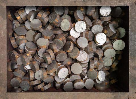 A pile of cutted with saw short cylindrical steel workpieces. Close-up abstract industrial background with rusted steel box frame.