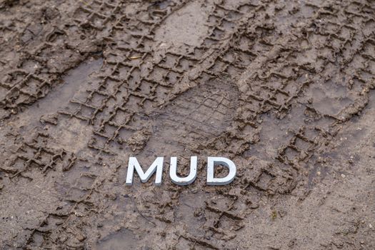 the word mud laid with silver metal letters on wet dirt surface with directly above perspective under cloudy autumn day light