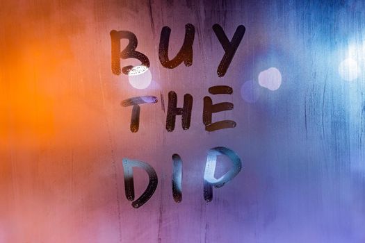 phrase buy the dip handwritten on night wet window glass surface - close-up with selective focus