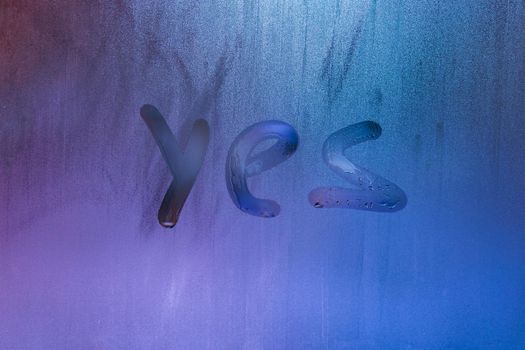 word yes handwritten on foggy night window glass surface, close-up with selective focus