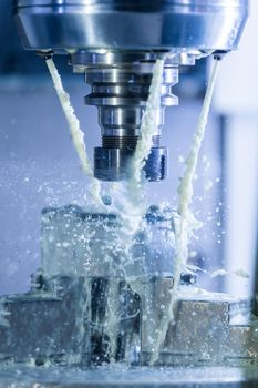 Vertical photo of industrial wet milling process in 5-axis cnc machine with coolant flow under pressure and freezed splashes.