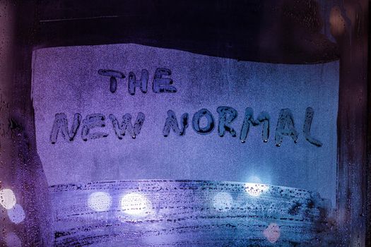 words the new normal handwritten on wet night window glass, close-up with selective focus