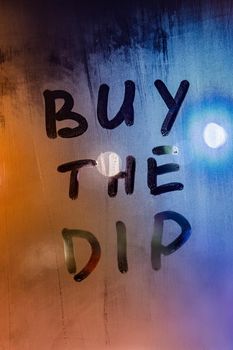 phrase buy the dip handwritten on night wet window glass surface - close-up with selective focus