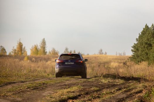 VOLKOVO, RUSSIA - OCTOBER 4, 2020: Blue Nissan Qashqai moving on dirt road in autumn field at day light. Russian country side.