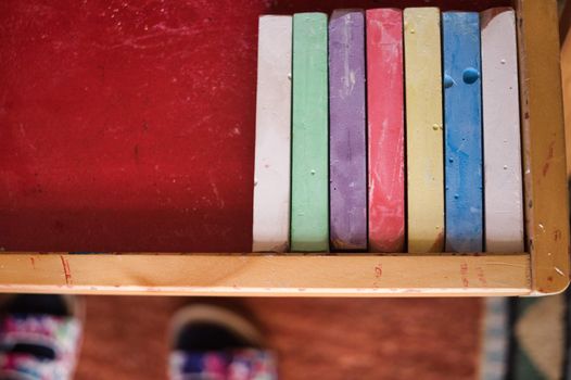 Colorful chalks on blackboard and kids shoes