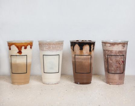 Cold chocolate drinks in plastic cups side by side, white background