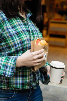 Woman holding sandwich and coffee cup