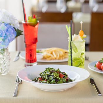 Salad with fried chicken french fries, red cocktail at restaurant