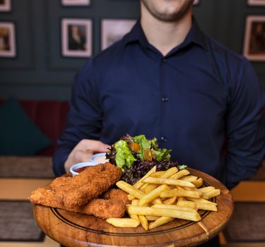 Waiter holding fried chicken and french fries on the wooden plate