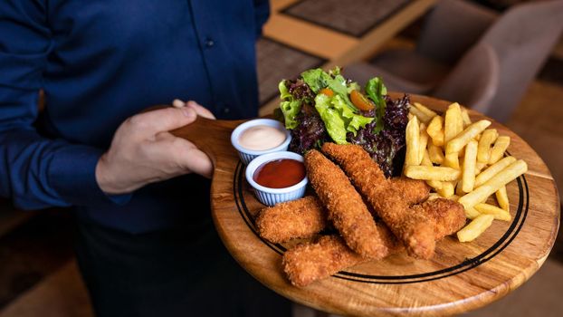 Waiter holding fried chicken and french fries on the wooden plate