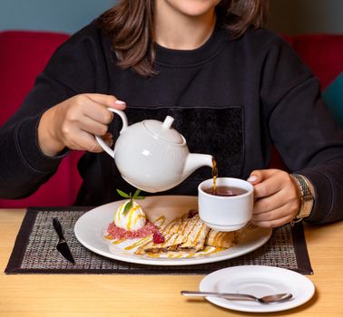 Woman pouring tea with dessert at restaurant