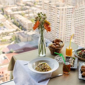 Pasta, salad, garnish, flower on the table with city view