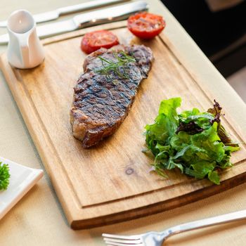 Tasty steak with vegetables on a wooden plate