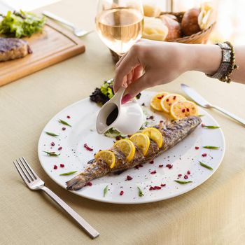 Woman pouring sauce to a fish meal with lemon