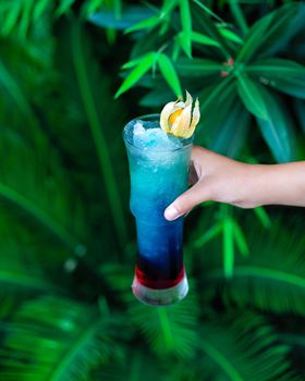 Woman holding blue colored cocktail with green background