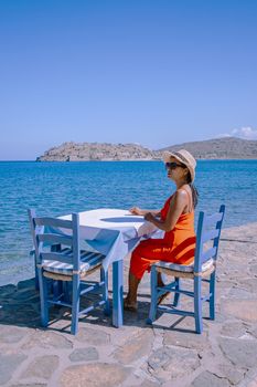 Crete Greece Plaka Lassithi with is traditional blue table and chairs and the beach in Crete Greece. Paralia Plakas, Plaka village Crete, young asian woman having lunch by the ocean