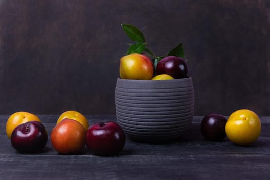Colorful plums fruit in pot and plate on the black background isolated