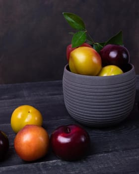 Colorful plums fruit in pot and plate on the black background isolated