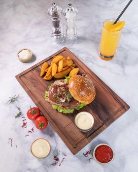 Tasty burger with fried potato, juice on wooden plate