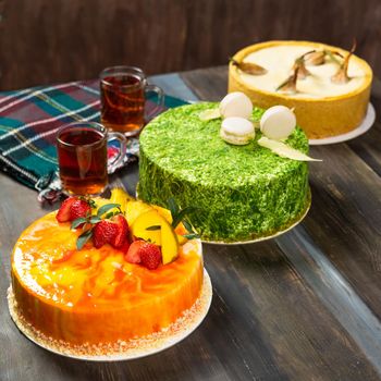 Different beautiful macaron, strawberry, pear cakes on the wooden table